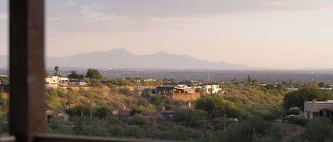 A view from a balcony overlooking a residential area with houses, trees, and distant mountains.