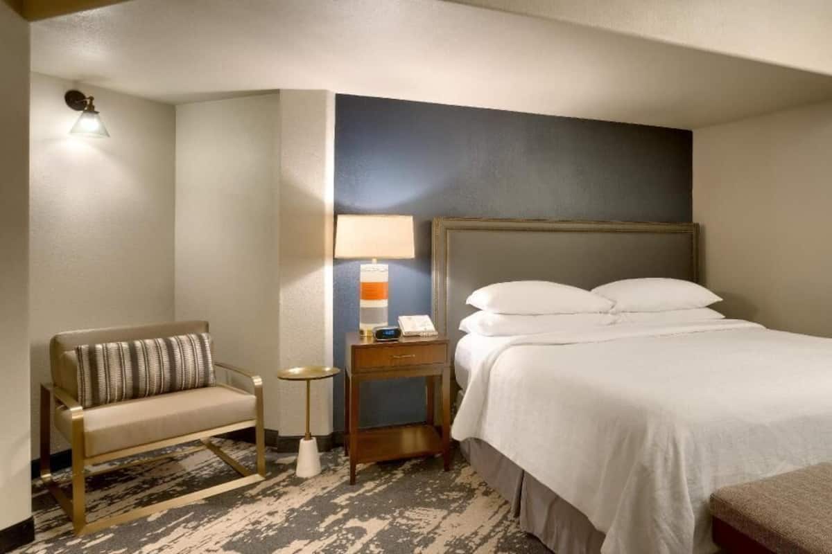 Une chambre d’hôtel comprenant un lit, un canapé, une table de chevet avec une lampe et un luminaire fixé au mur.