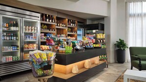 Een hotel lobby met een receptiebalie, planken vol snacks en drankjes, en een koelkast met drank.