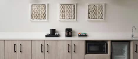 A modern kitchen with light wood cabinets, a built-in microwave, and a refrigerator with a glass door. Three pendant lights hang above the counter.