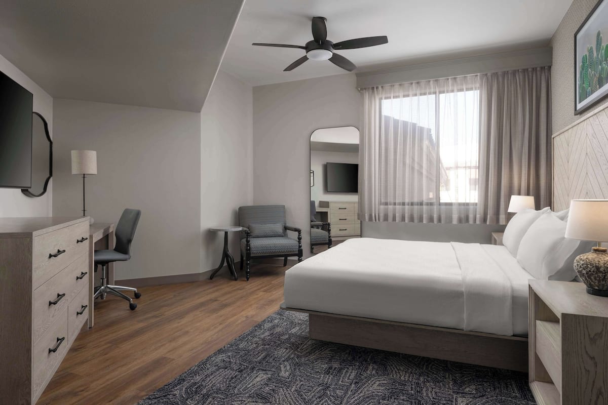 Une chambre d’hôtel moderne équipée d’un grand lit, d’un bureau, d’une chaise, d’un ventilateur de plafond, d’une télévision et d’une fenêtre avec des rideaux.