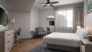 A modern hotel room with a large bed, a desk, a chair, a ceiling fan, a TV, and a window with curtains.
