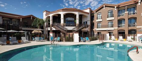 A swimming pool with lounge chairs and a staircase leading to a building with balconies.