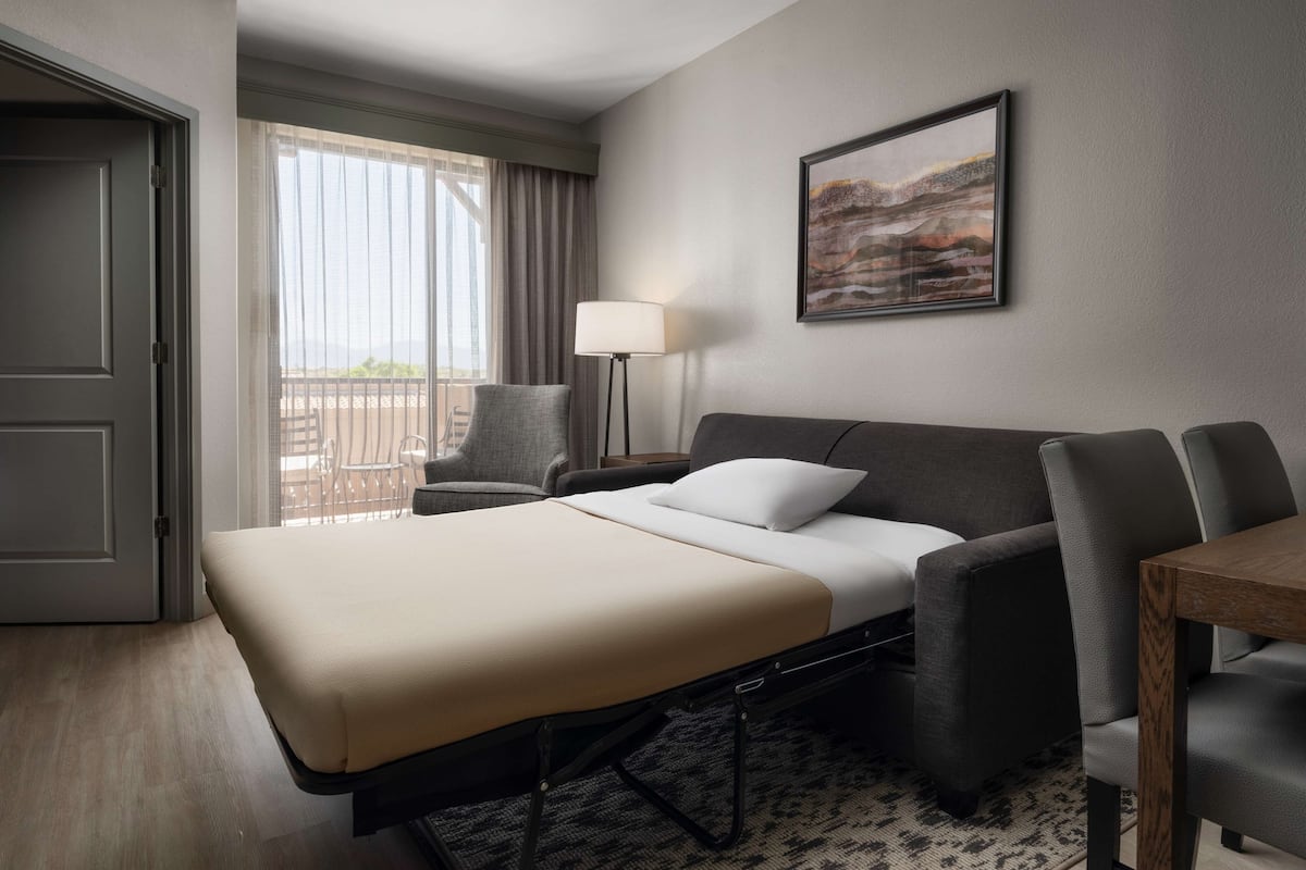 Une chambre d’hôtel avec un lit, un bureau, une chaise, une lampe et un balcon avec vue.