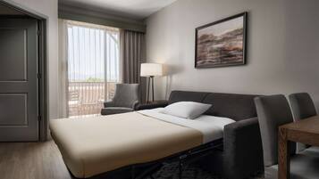Ein Hotelzimmer mit Bett, Schreibtisch, Stuhl, Lampe und einem Balkon mit Blick.