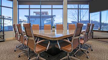 A conference room with a large oval table, six brown leather chairs, and large windows offering a view of buildings and trees.
