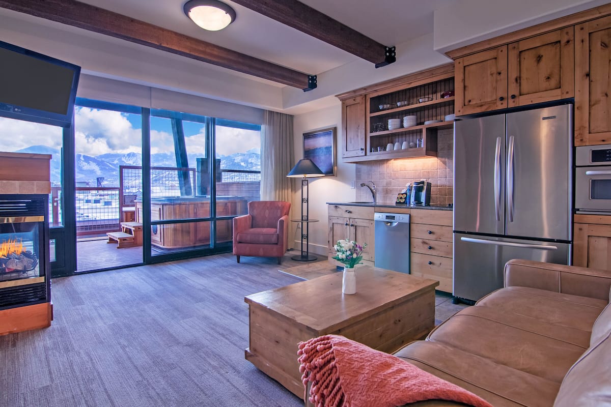 A modern kitchen with wooden cabinets, a stainless steel refrigerator, and a dining area with a wooden table and chairs.