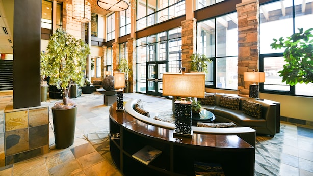 A spacious lobby with a curved reception desk, large windows, and several potted plants. - Newpark Resort (Park City)