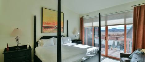 Una cama con dosel y vistas a la ciudad, una mesita de noche con lámpara, y una ventana con persianas.