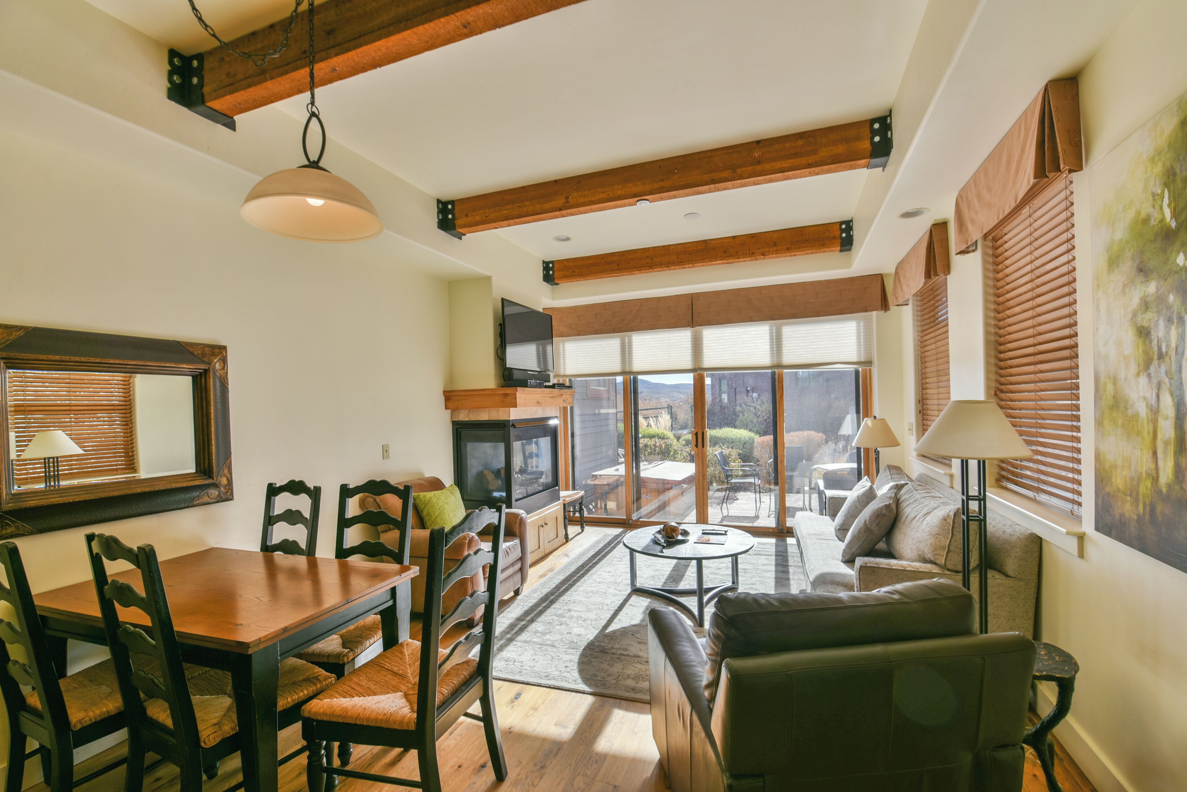 Un salón amplio con una mesa de comedor de madera, asientos cómodos, una chimenea y ventanas grandes que ofrecen vistas al exterior.