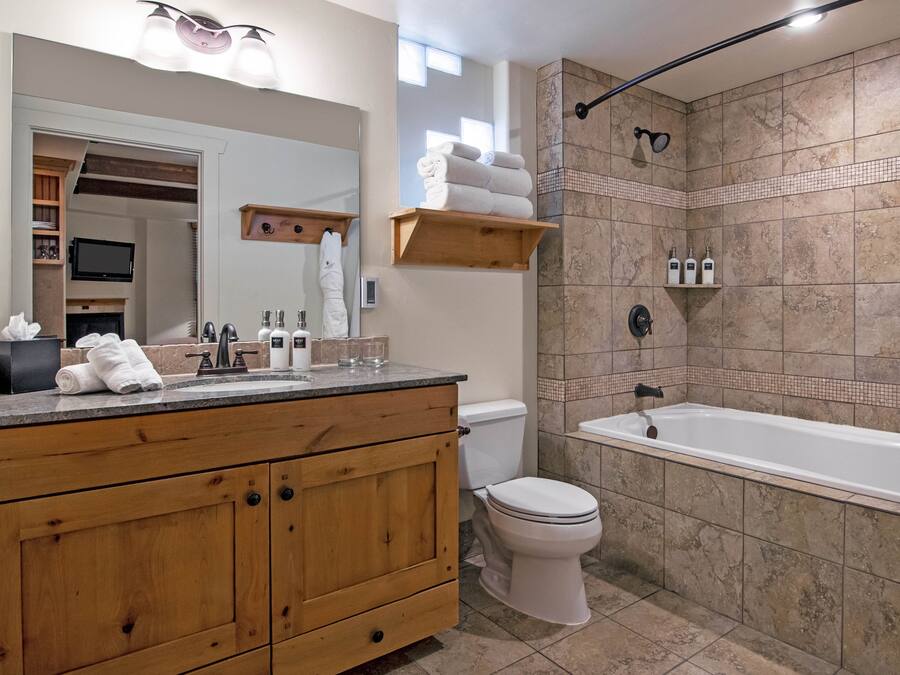 A modern bathroom with a wooden vanity, a toilet, a bathtub, and a shower area.