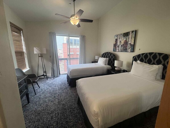 A hotel room with two beds, a desk, a chair, a ceiling fan, and a window with blinds. - Newpark Resort (Park City)