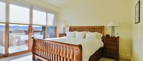 Une chambre à coucher avec un grand lit, deux tables de chevet, une petite table et une vue dégagée sur l’extérieur grâce à une grande fenêtre.