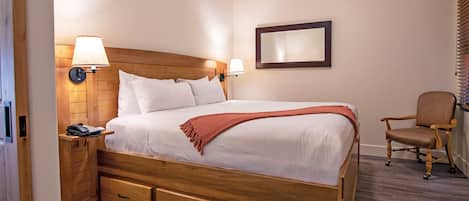 A hotel room with a wooden bed, bedside lamps, a desk with a phone, a chair, and a mirror on the wall.