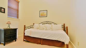 A bedroom with a bed, a nightstand, a lamp, a window with blinds, and a framed picture on the wall.
