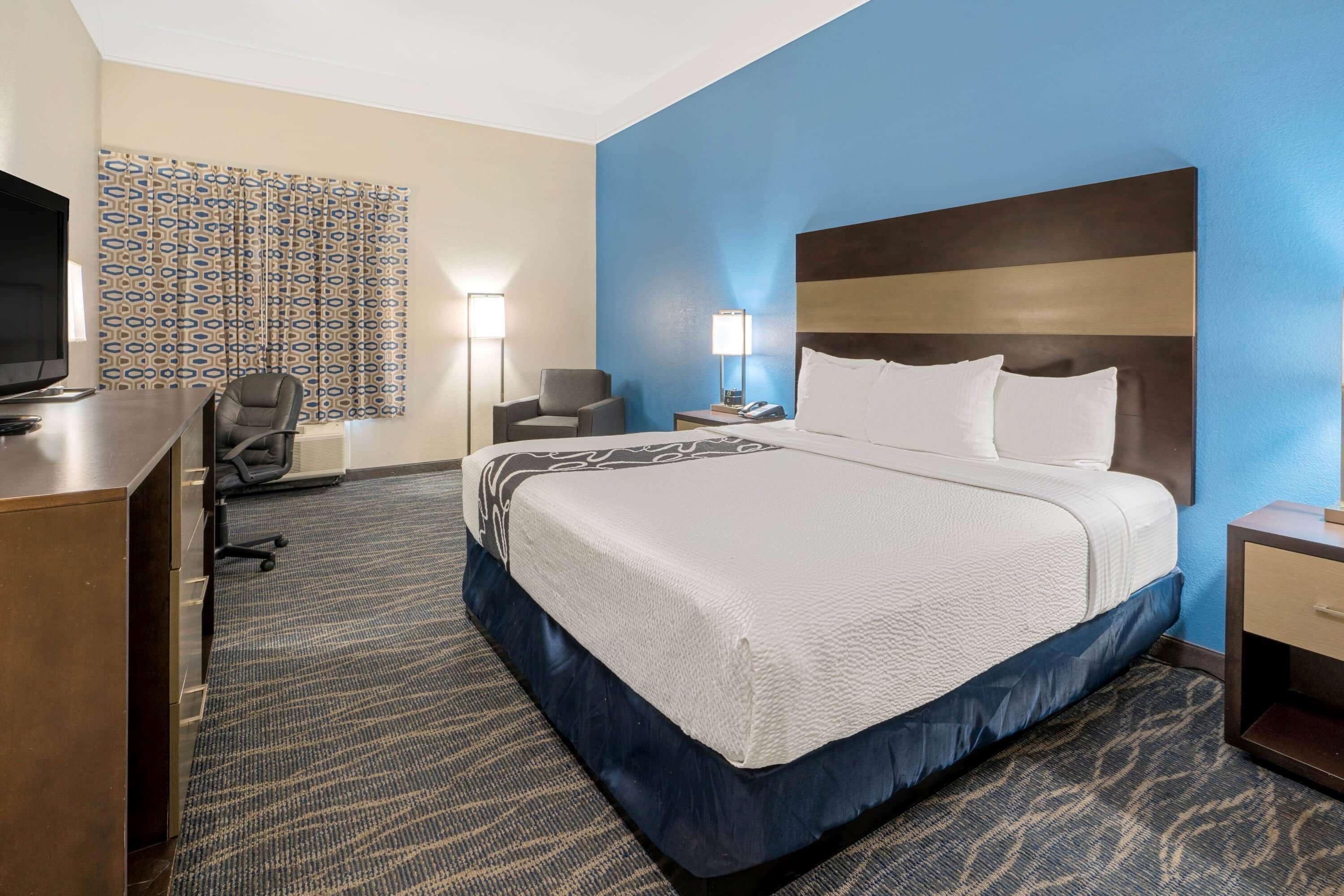 Une chambre d’hôtel avec un grand lit, un bureau, une chaise, une télévision et un rideau à motifs.