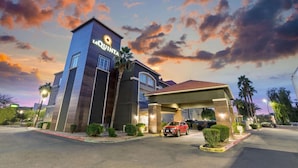 Un hotel de diseño moderno, con una torre destacada que muestra el nombre de la marca, una entrada cubierta y un área de estacionamiento.