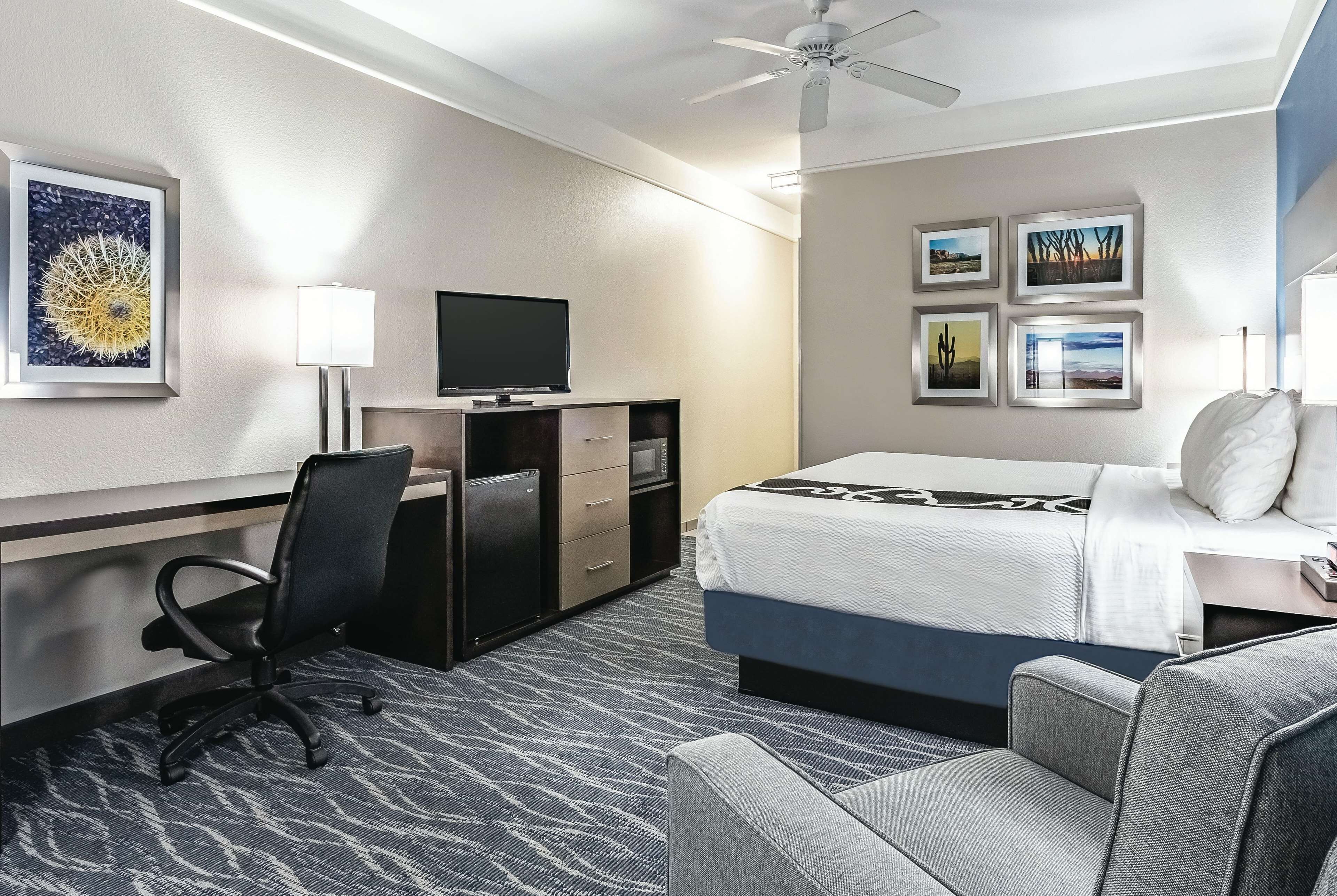 A hotel room with a bed, a desk with a computer, a chair, a TV, and artwork on the walls.