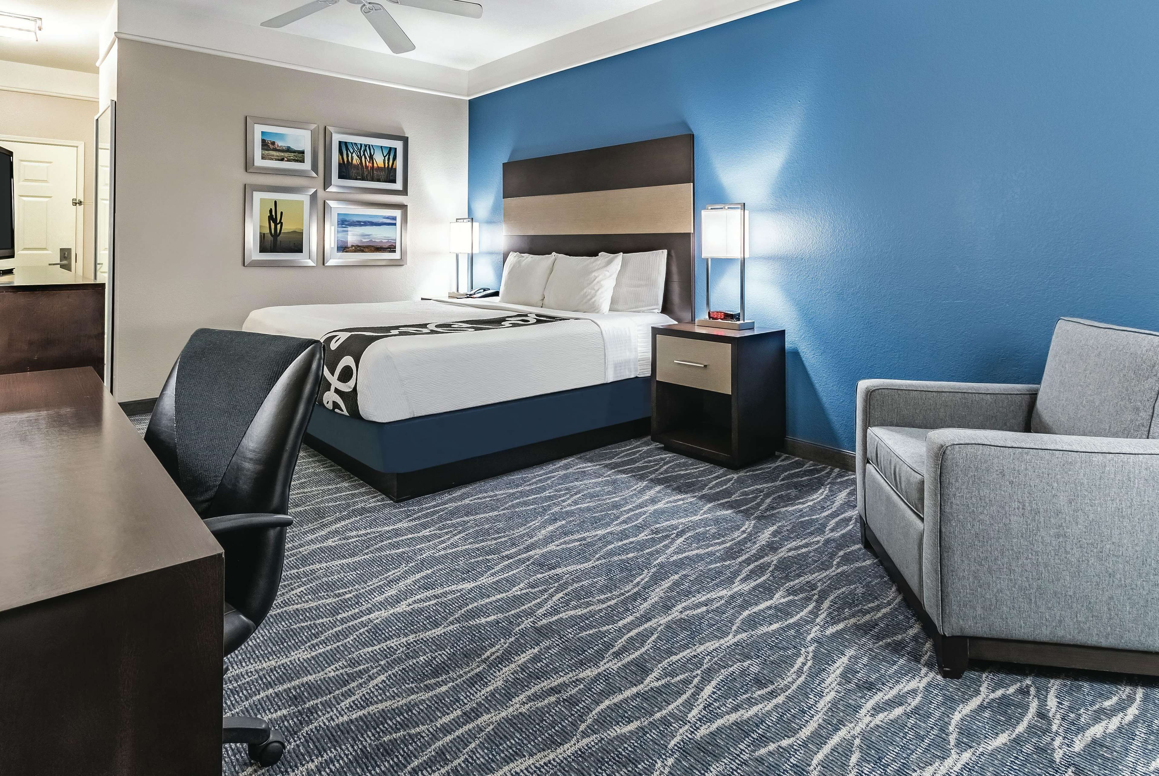Una habitación de hotel con cama, escritorio, silla y mesita de noche con lámpara.