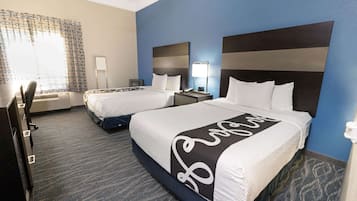 Ein Hotelzimmer mit zwei Betten, einem Schreibtisch, einem Stuhl, einer Lampe und einem Fenster mit gemusterten Vorhängen.