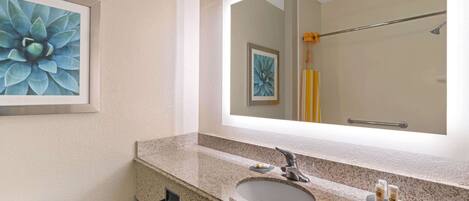 A bathroom with a granite countertop, a sink, a mirror, and a framed floral artwork.