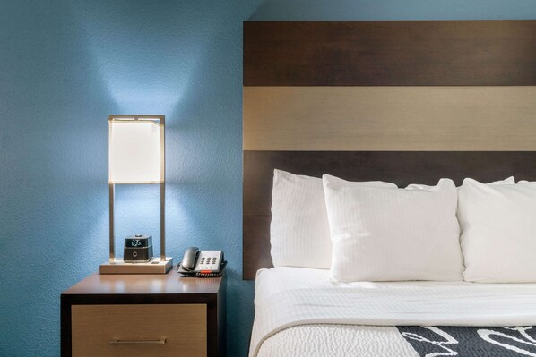 Una habitación de hotel con una cama, una mesita de noche con una lámpara, un teléfono y una cajita.