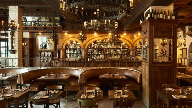 A restaurant with wooden interiors, a bar area, and a variety of seating options including booths and tables. - The Bowery Hotel (New York)