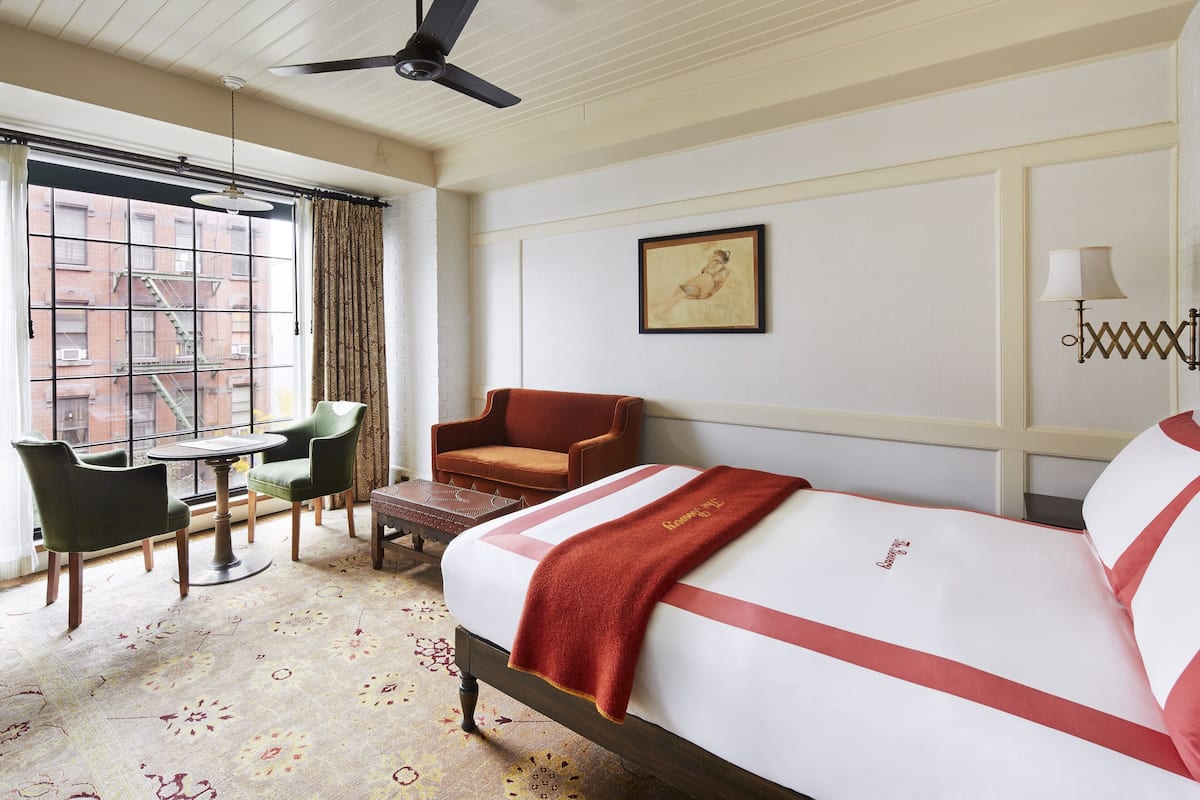 A hotel room with a bed, a chair, a table, and a window with a view of buildings.