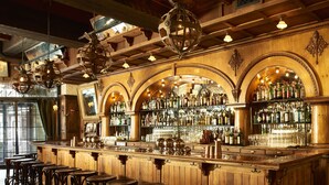 A bar with wooden bar stools, a well-stocked liquor shelf, and decorative globes on the ceiling.
