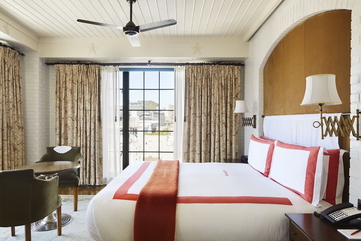 A hotel room with a large bed, a desk, a chair, and a view of the city through the window.