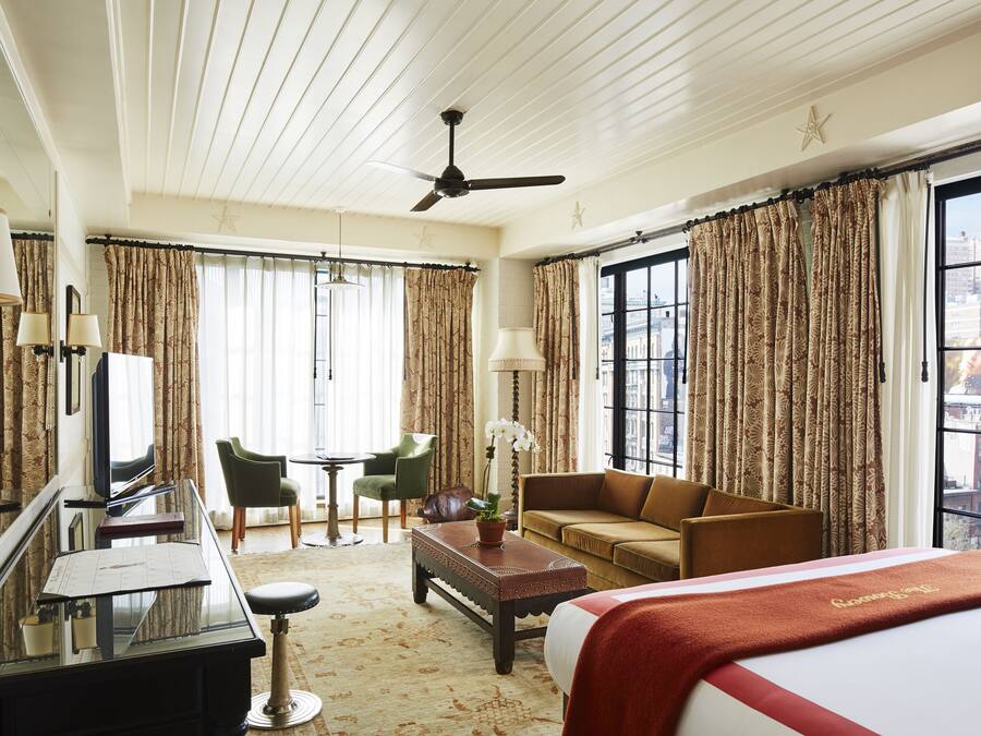 Una habitación de hotel con cama, escritorio, silla, sofá, mesa de centro y televisión.