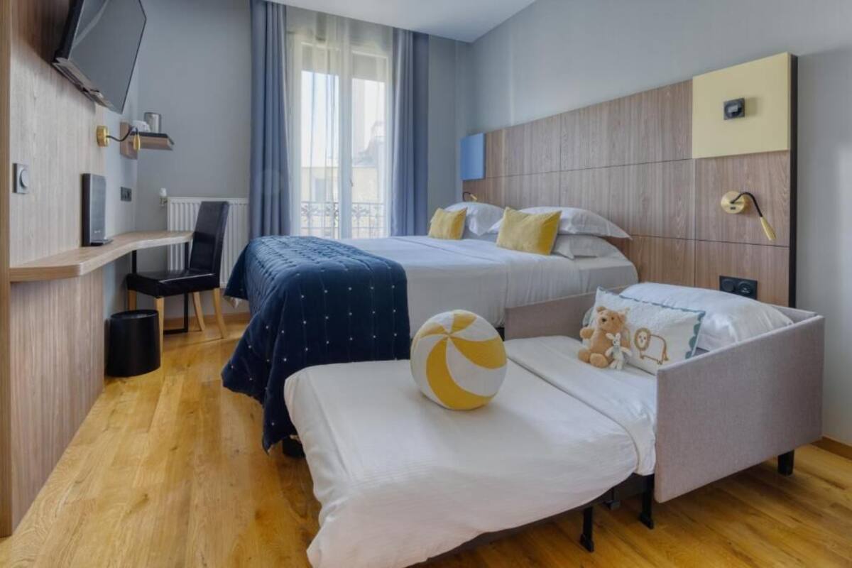 Habitación de hotel con cama, escritorio, silla, televisor y ventana con cortinas.