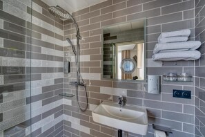Un baño moderno con cabina de ducha de vidrio, un lavamanos, un espejo y toallas ordenadas.