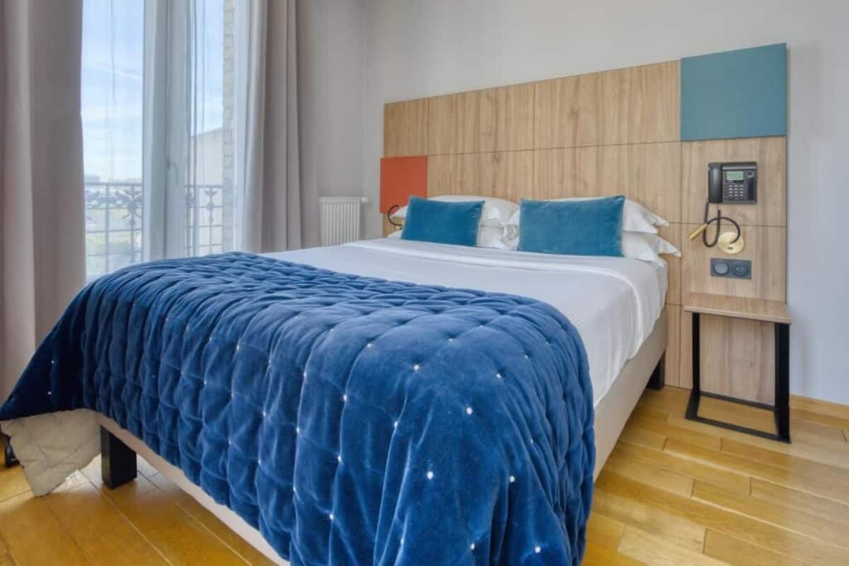 Habitación de hotel con una cama grande, cabecera de madera, teléfono en la mesita de noche y vistas al exterior.