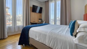 Habitación de hotel con una cama grande, un escritorio, un televisor y vistas al balcón.