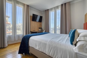 Una camera d'albergo con un letto grande, una scrivania, una TV e vista su un balcone.
