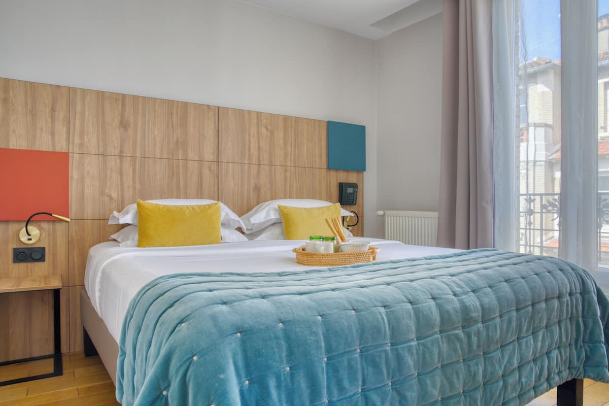 Una habitación de hotel con cama, cabecero de madera, teléfono y ventana con vistas.