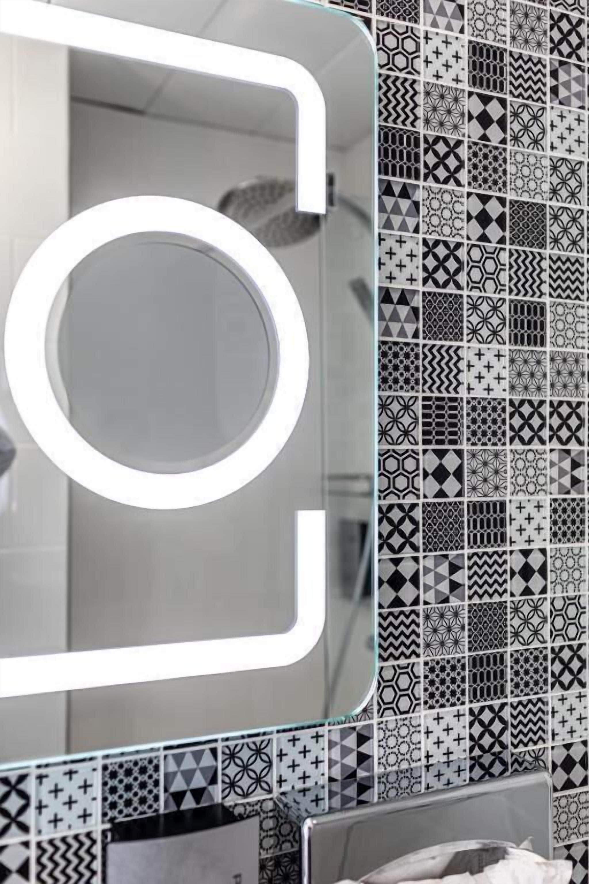 A bathroom with a mirror, a sink, and a tiled wall with various geometric patterns.