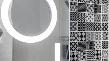 A bathroom with a mirror, a sink, and a tiled wall with various geometric patterns.