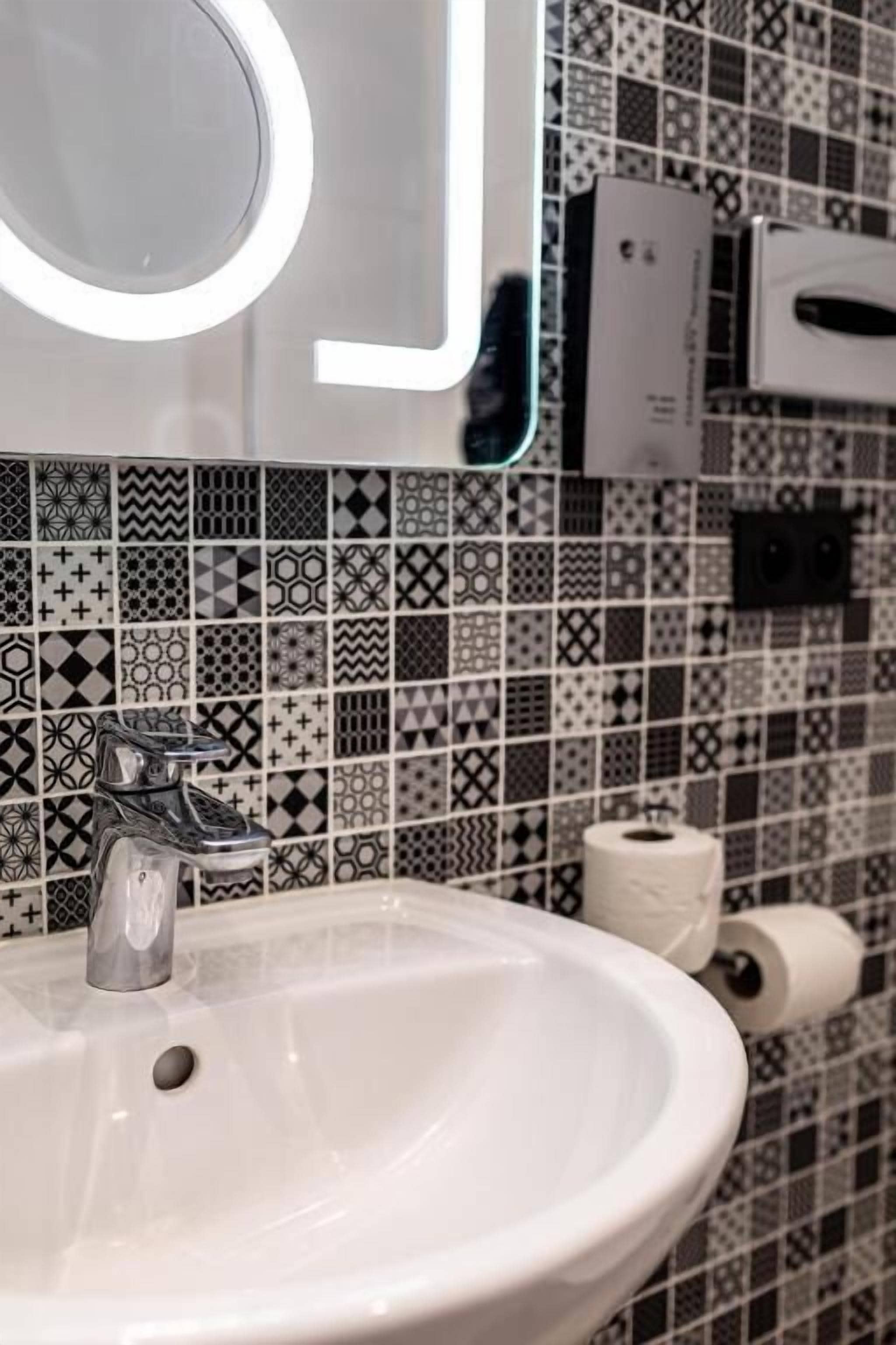 A bathroom with a white sink, a mirror, and a patterned tile backsplash.