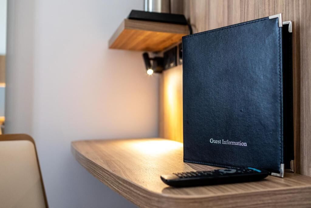 A black leather-bound notebook labeled "Guest Information" on a wooden table with a remote control beside it.