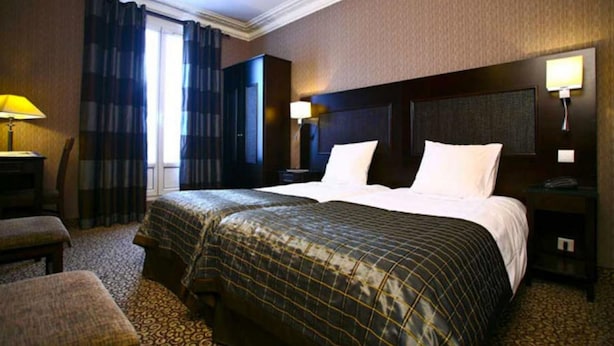 Una habitación de hotel con una cama grande, dos mesitas de noche, un escritorio, una silla y una ventana con cortinas.