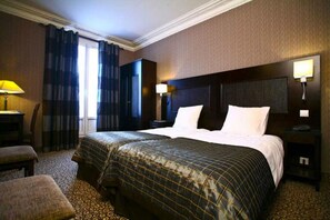 A hotel room with a large bed, two bedside tables, a desk, a chair, and a window with curtains. - Hotel Convention Montparnasse (Paris)
