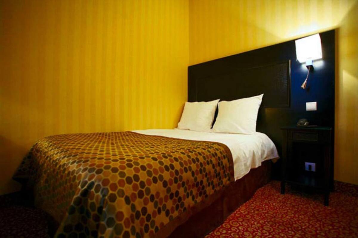 A hotel room with a bed, a nightstand, and a wall-mounted lamp.