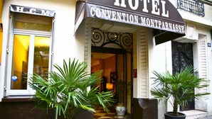 Entrada de un hotel con un cartel que dice 'HOTEL CONVENTION MONTPARNASSE'. Hay dos plantas en macetas frente a la entrada.