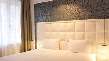 A hotel room with a large bed, a headboard with a light panel, a bedside table, and a patterned wallpaper.