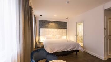 A bedroom with a large bed, a chair, a bedside table, and a door.