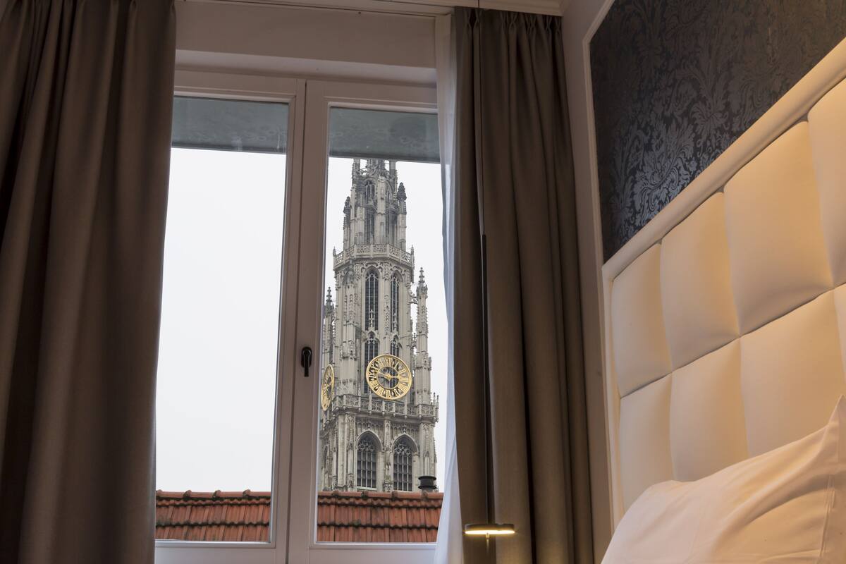 Een kamer met een groot raam, een bed en uitzicht op een historisch gebouw.