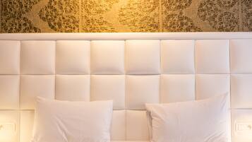 Quarto de hotel com cabeceira acolchoada, duas almofadas brancas e parede estampada.