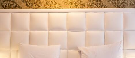 A hotel room with a tufted headboard, two white pillows, and a patterned wall.